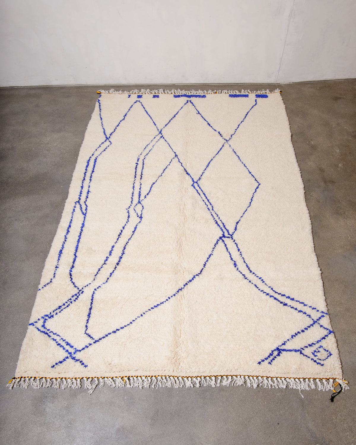 Berberlin wool Azilal rug in cream with a blue abstract design laying on concrete floor.
